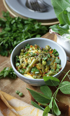 Vegan protein meal, dish of assorted stewed green legume vegetables: peas, green bean, broccoli garnished with parsley and flower petals, closep, vertical, vegan food concept, from above top down view