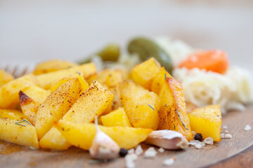 Roasted potatoes seasoned with salt, herbs and paprika on wooden board. Roast potato with pickles and sauerkraut.