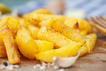 Roasted potatoes seasoned with salt, herbs and paprika on wooden board.