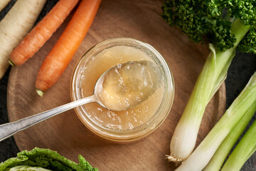 Chilled jellied beef bone broth on a spoon, with fresh vegetables - obrazy, fototapety, plakaty