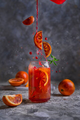 Red orange juice refreshing drink, splashing in a glass, grey textured background with fresh fruits.  Copy space.