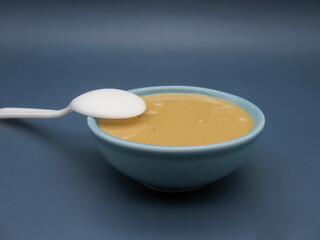 White teaspoon in peanut paste in a blue small bowl on a blue background