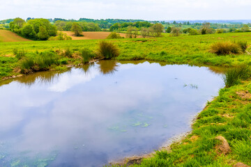 Fototapeta na wymiar A view across a dew pond towards the village of Gumley near Market Harborough, UK in springtime
