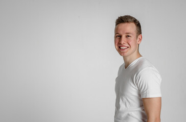 teen guy looking at camera happy
 and smiling with teeth in the right side of the frame on a white background in a white T-shirt
