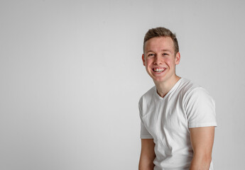 
teen guy looking at camera happy
 and sincerely smiling with teeth in the right side of the frame on a white background in a white T-shirt