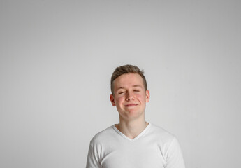 
teen guy looking at camera closed his eyes happy
 and sincerely smiling with teeth on a white background in a white T-shirt