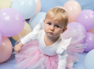 Obraz na płótnie Canvas A beautiful little girl 1 year old in pink tutu skirt among balloons looks up at the camera
