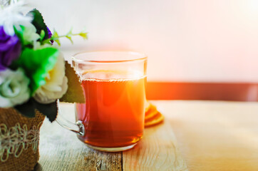 Hot tea in glass cup on a wooden table in the rays of sunlight.