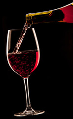 Fototapeta na wymiar Pouring a glass of red wine on black background.