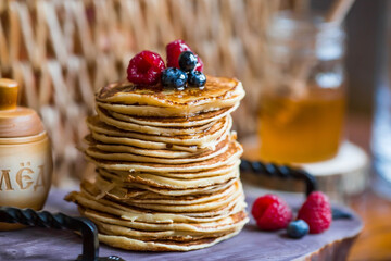 Delicious pancakes with honey, blueberries and raspberries. Next to it is a wooden barrel with an...