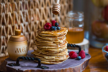 Delicious pancakes with honey, blueberries and raspberries. Next to it is a wooden barrel with an...