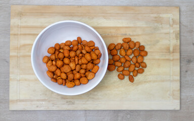 Crispy peanuts roasted in the oven with red pepper in a bowl on a kitchen board on a table with different textures. Snack widely used in meetings of friends.