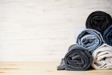 Pile of jeans on light wooden background, space for text.