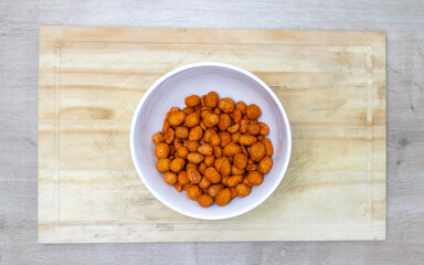 Crispy peanuts roasted in the oven with red pepper in a bowl on a kitchen board on a table with different textures. Snack widely used in meetings of friends.