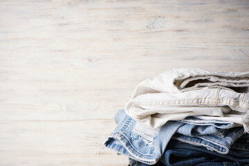 Jeans pants stack on light wooden background, place for text.