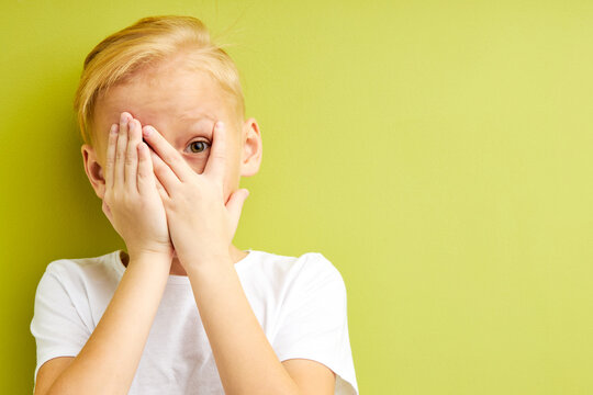 Scared Kid Boy Covering Eyes And Mouth With Hands, Frightened And Shocked By Something, Hiding Emotions. Isolated Green Background