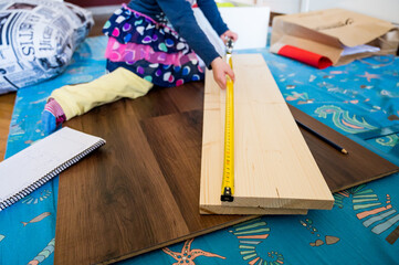 Detail of child helping with measuring wooden plank to make shelves.