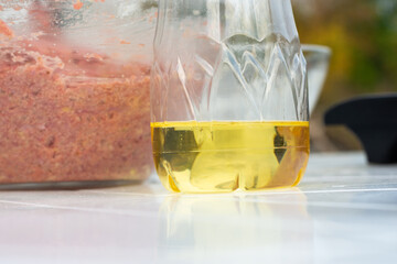On the table is sunflower oil in a plastic bottle, in the background is a glass bowl with minced...