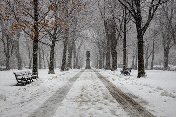 Statue on a snowy path with snow falling and tire tracks