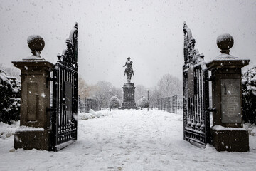 George Washington statue in the Boston Commons during a snow storm framed by open gates