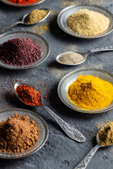 Assortment of natural spices on a vintage silver spoons or dishes on dark rustic stone background, Healthy spice concept