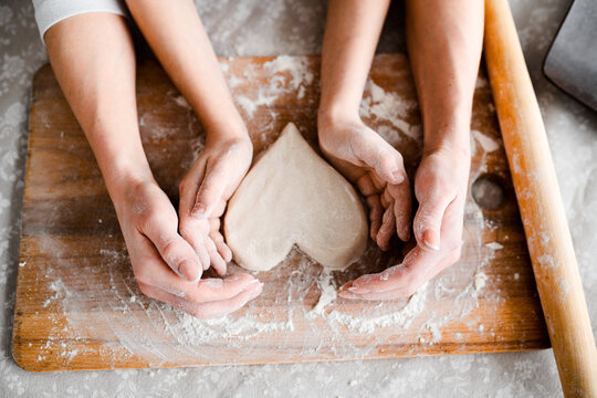 Top view, hands close-up. Mom and daughter make cookies in the form of Wednesday, together roll out the heart with a rolling pin on a wooden board in flour
