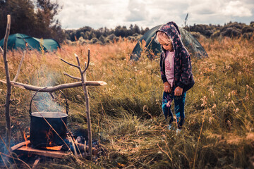 Child girl on camping site in rural field with fire on field kitchen concept for adventure family lifestyle