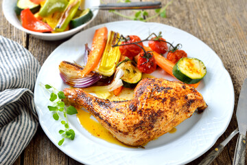Knusprig gebackene Hühnerkeule mit mediterranem Gemüse heiß auf einem Porzellanteller  serviert – Crispy oven roasted chicken leg with colorful mediterranean vegetables hot served on a white plate