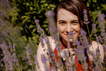 Woman sitting near the bushes of lavender. Enjoy on the floral glade, summer nature. Beautiful girl in dress on purple the lavender field. Happy girl smiles against a flowering field of lavender.