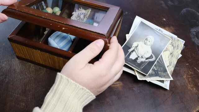 female hands are sorting dear to heart memorabilia in an old wooden box, rosary, a stack of retro photos, vintage photographs of 1960, concept of family tree, genealogy, connection with ancestors