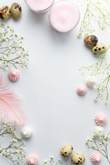 Fototapeta na wymiar Beautiful festive Easter frame made with little white flowers, quail eggs, feathers and merengue cookies on light grey background. Copy space for your design. Eco friendly holiday decorations.