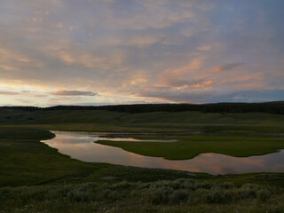 View of a river flowing through a meadow at Yellowstone National Park at sunset, with reflections of colorful clouds in the water