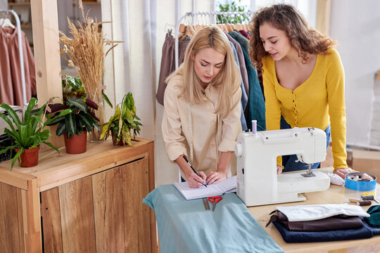 tailor discuss clothes sketch with interested female client, caucasian fashion designers team negotiate about new collection, talking about fabrics and patterns in modern design studio or workshop - Powered by Adobe