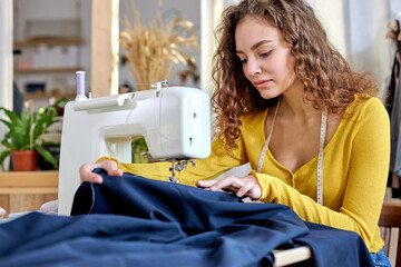 young tailor working on sewing machine, hand making clothes in home interior. caucasian curly...