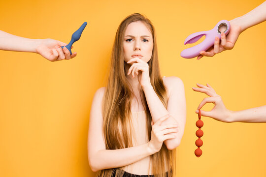 The Caucasian woman portrays a pensive view of an abundance of dildos or clitoral masters. Selection of toys for adults, sex shop concept