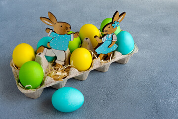 Multicolor easter eggs with easter bunnies in egg carton on grey background