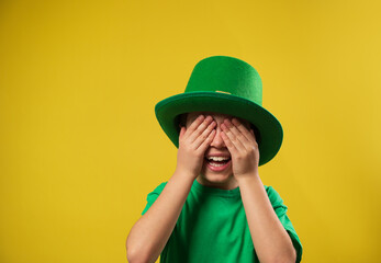 Little laughing boy in green Irish leprechaun hat covers his eyes with his palms. Saint Patrick Day...