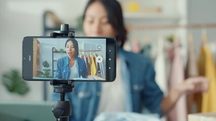 Young Asia lady fashion designer using mobile phone receiving purchase order and showing clothes recording video live streaming online at shop. Small business owner, online market delivery concept. - Powered by Adobe
