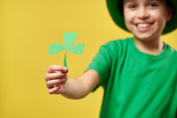 Focus on child's hand holding a clover leaf isolated on yellow background. Saint Patrick Day. Copy space