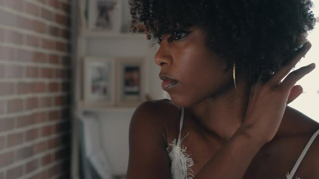 Beautiful black woman with afro brushing through her curls while looking at the mirror