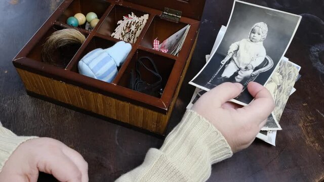 female hands are sorting dear to heart memorabilia in an old wooden box, a stack of retro photos, vintage photographs of 1960, concept of family tree, genealogy, connection with ancestors