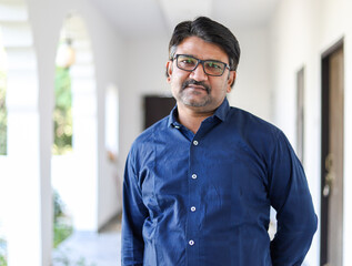 Portrait of a middle-aged Indian male with eyeglasses wearing a blue shirt