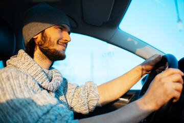 Portrait of smiling young man driving the car. Wearing hat and sweater.