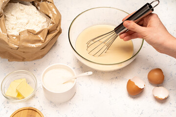 the process of making dough for pancakes with ingredients on a light table, eggs and flour are whipped with a mixer