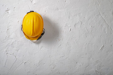 Yellow work helmet hung on a hook. Health and safety accessories on a white wall background.