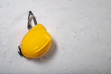 Yellow work helmet hung on a hook. Health and safety accessories on a white wall background.