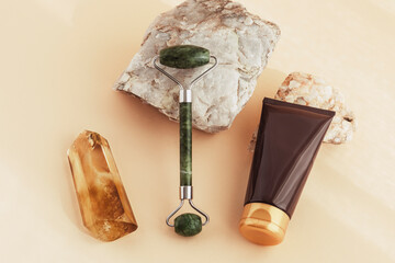 Beauty products, facial roller, cream and crystal on yellow background. Top view