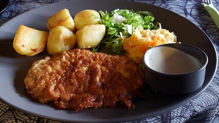 Large pork chop with boiled potatoes and fresh salad on a plate
