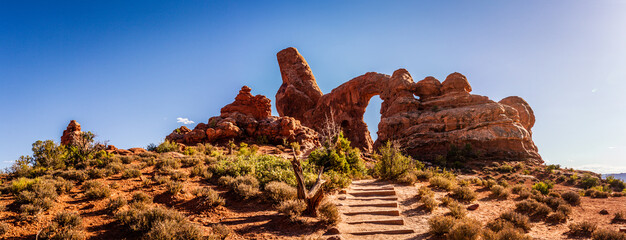 Panoram shot of steps to red sandstone arch, rock window and monolith in stone sculpture in arches...