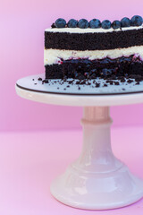 Chocolate sponge cake with a layer of cheese cream. Decorated with blueberries. Delicious wedding cake. Cake on a pink isolated background.